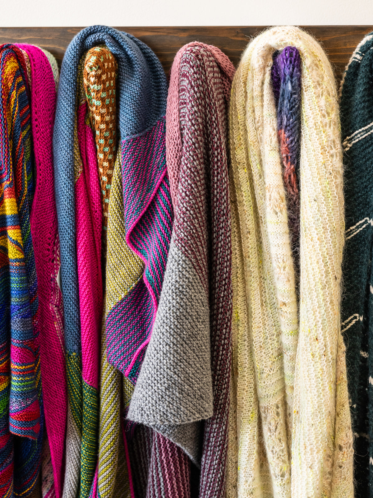 Collection of colorful knitted scarves hanging on a rack.