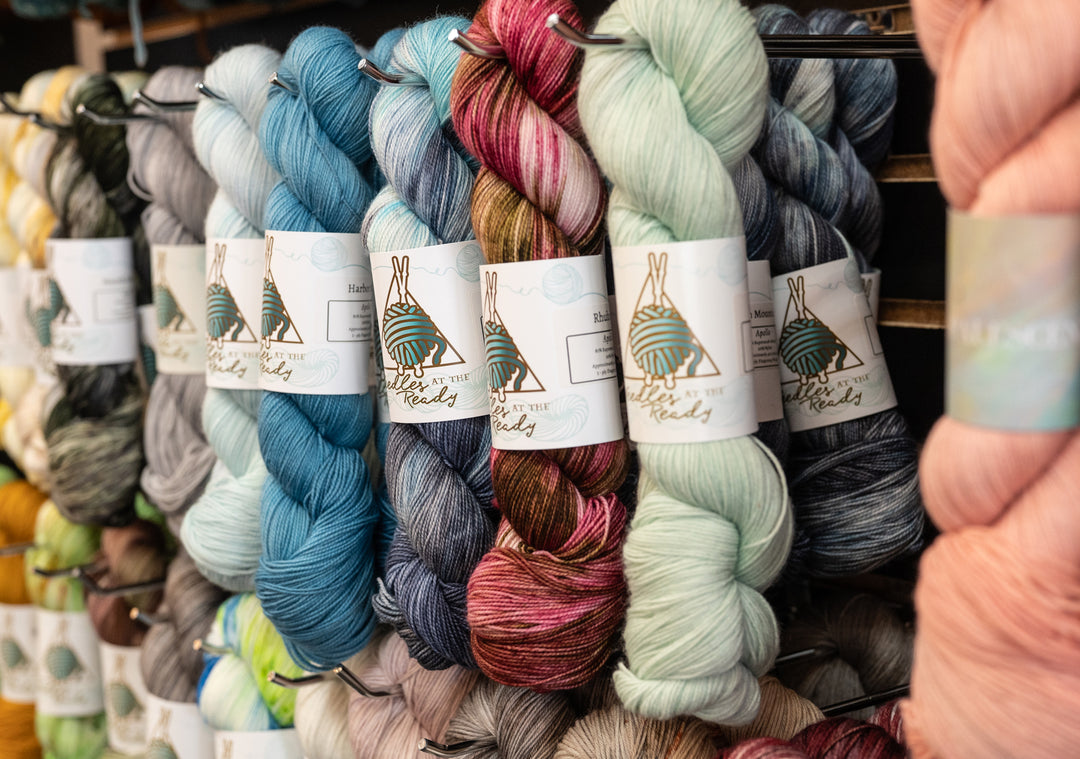 Colorful yarn skeins with labels on a rack, held by a hand.