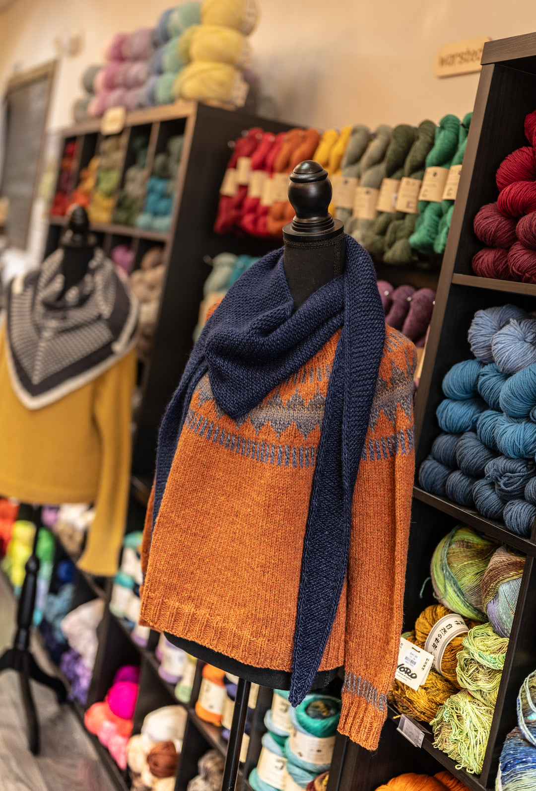 Hand-knit orange sweater and blue scarf displayed at Skein Yarn Shop