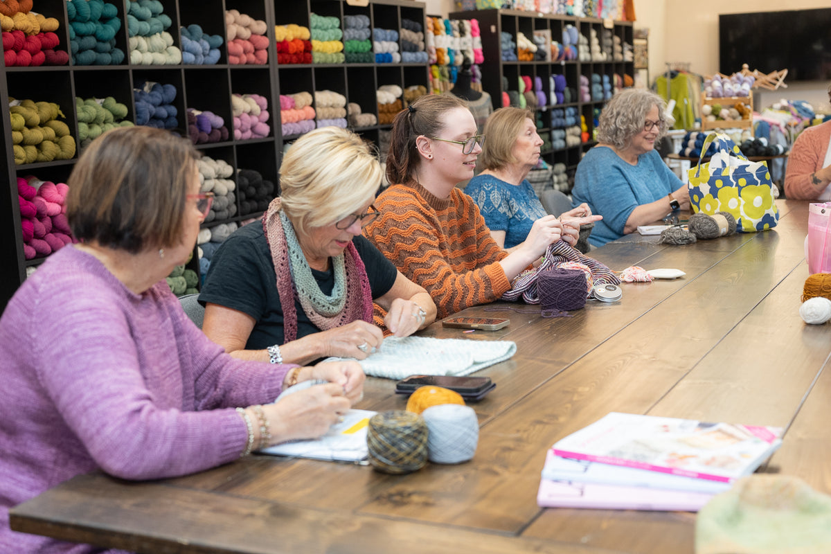 Group of women knitting together at the community table at Skein Yarn Shop