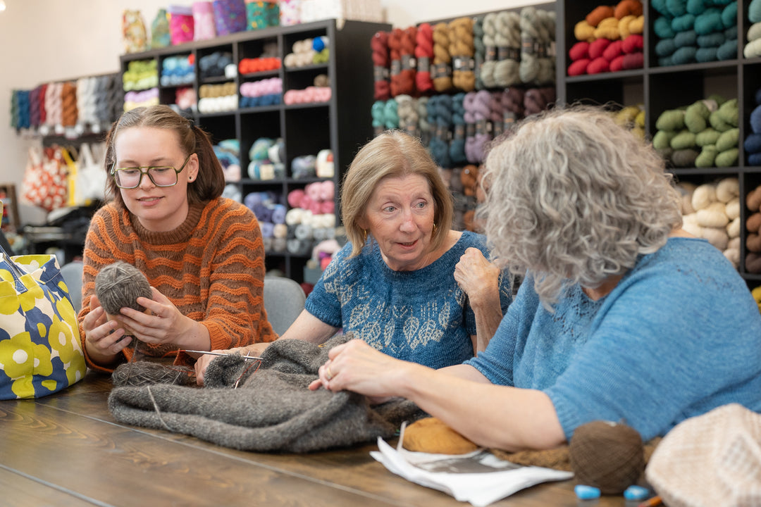 Three women in Skein yarn shop examining yarn and knitting materials.