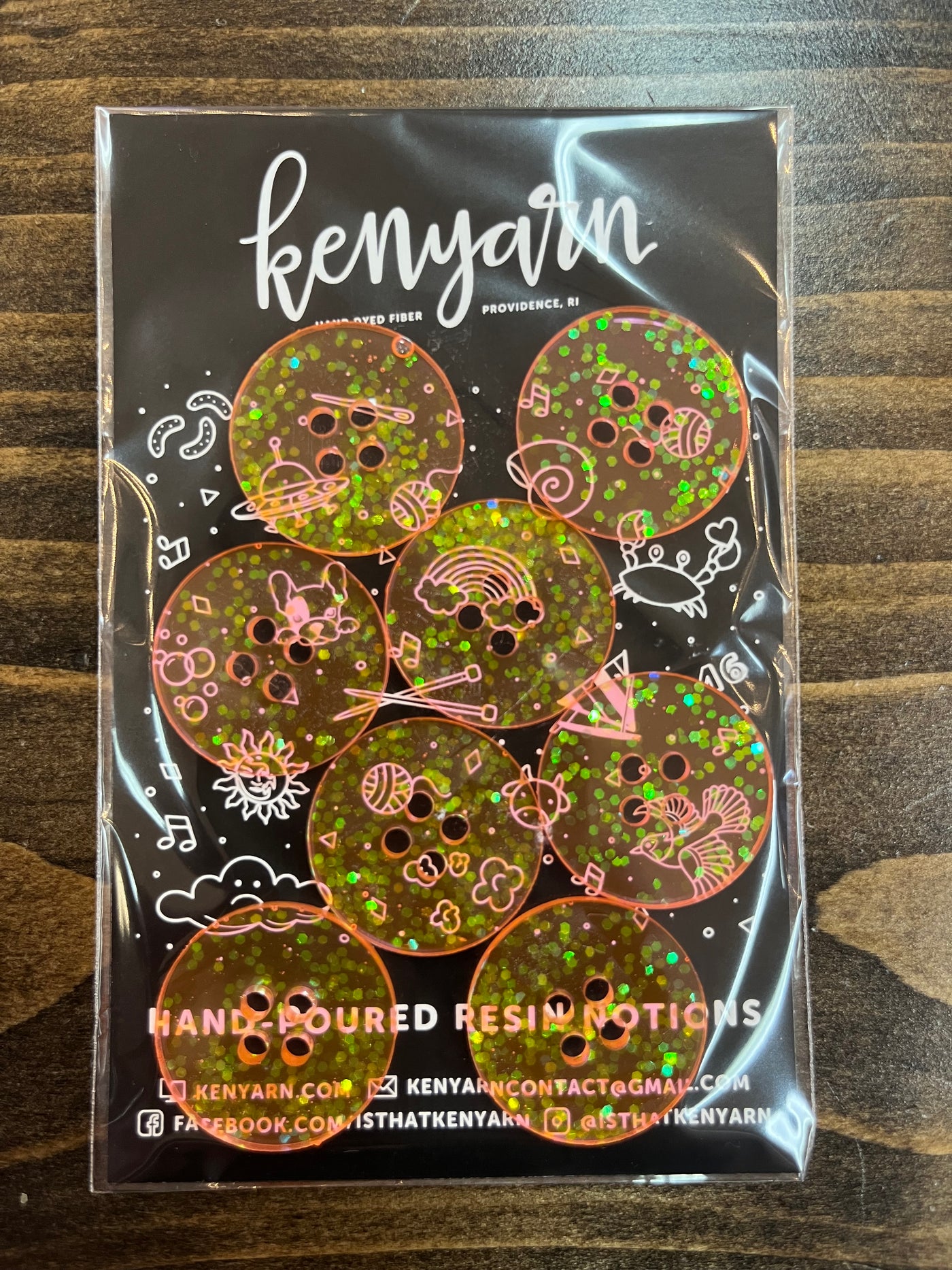 A 1-inch circle resin button in translucent peach color with green sparkles inside. The packaging reads "Kenyarn."