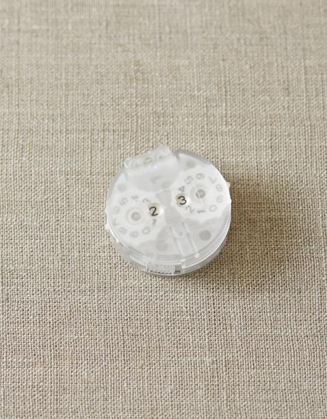 A knitting or crochet row counter that is a small piece of round translucent plastic with two scrolling number wheels inside.