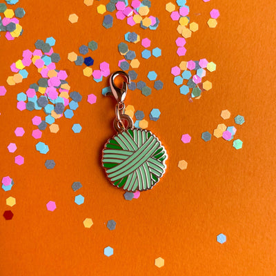 A mint green yarn ball charm on an orange background covered in confetti