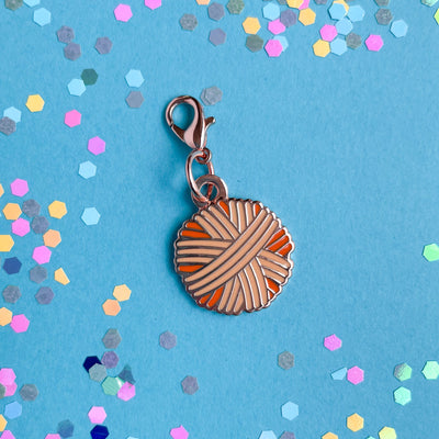 A yarn ball shaped lobster claw clasp charm on a blue paper background with confetti on it. 