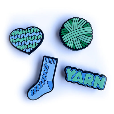 PVC charms shaped like a heart, a sock, a yarn ball and the word yarn in shades of mint green and pastel blue. 