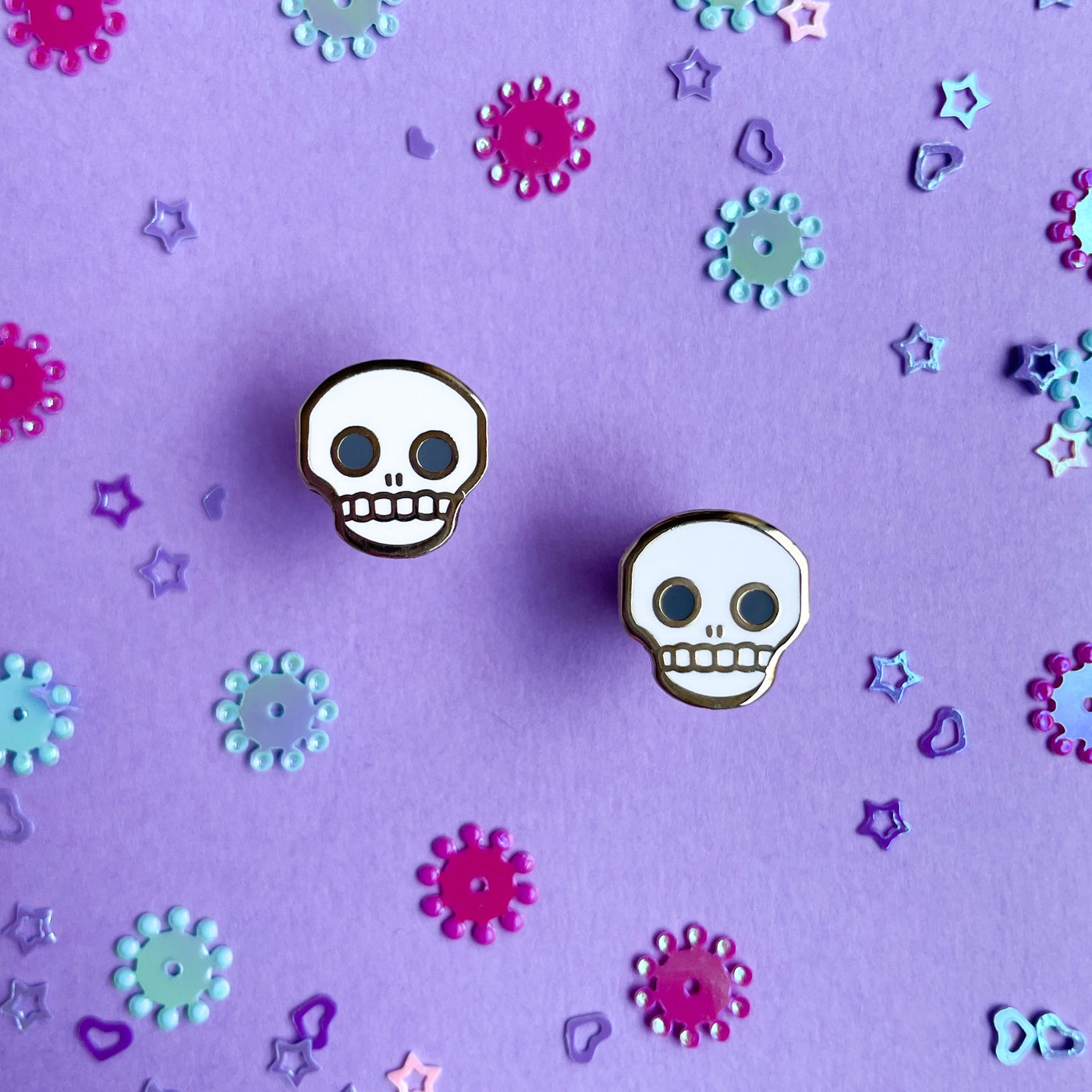 Stud earrings shaped like skulls on a purple background. 