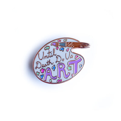 An enamel pin shaped like an artist's palette with a paint brush that reads "until death do us art".