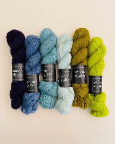 Skeins of fluffy cashmere yarn in hues of dark blue to neon green arranged in a line together from blue to green.