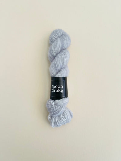 A fluffy grey sweatshirt colored skein of luxury yarn with a black label that reads "Moondrake Co"