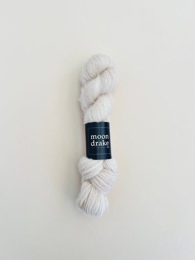 An eggshell white skein of fingering weight yarn with an airy light texture.