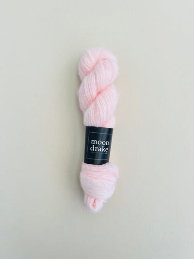 A powder pink skein of brushed cashmere merino yarn with a black label.
