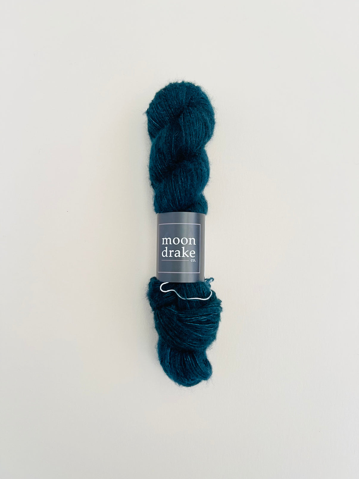 A deep teal colored skein of fuzzy textured yarn.