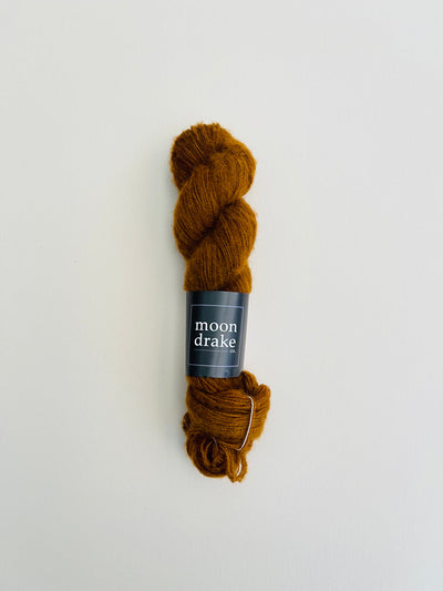 A warm brown skein of brushed cashmere yarn with a black label that reads "Moondrake Co"
