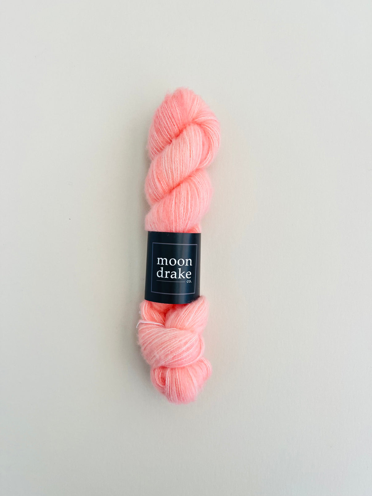 A coral skein of fuzzy textured yarn with a black label that reads "Moon Drake Co"