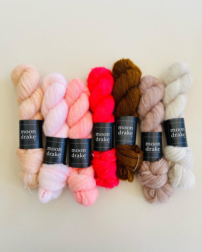 Seven skeins of floofy cashmere yarn in various shades of warm neutrals and pinks. The yarn has a very fluffy halo texture.